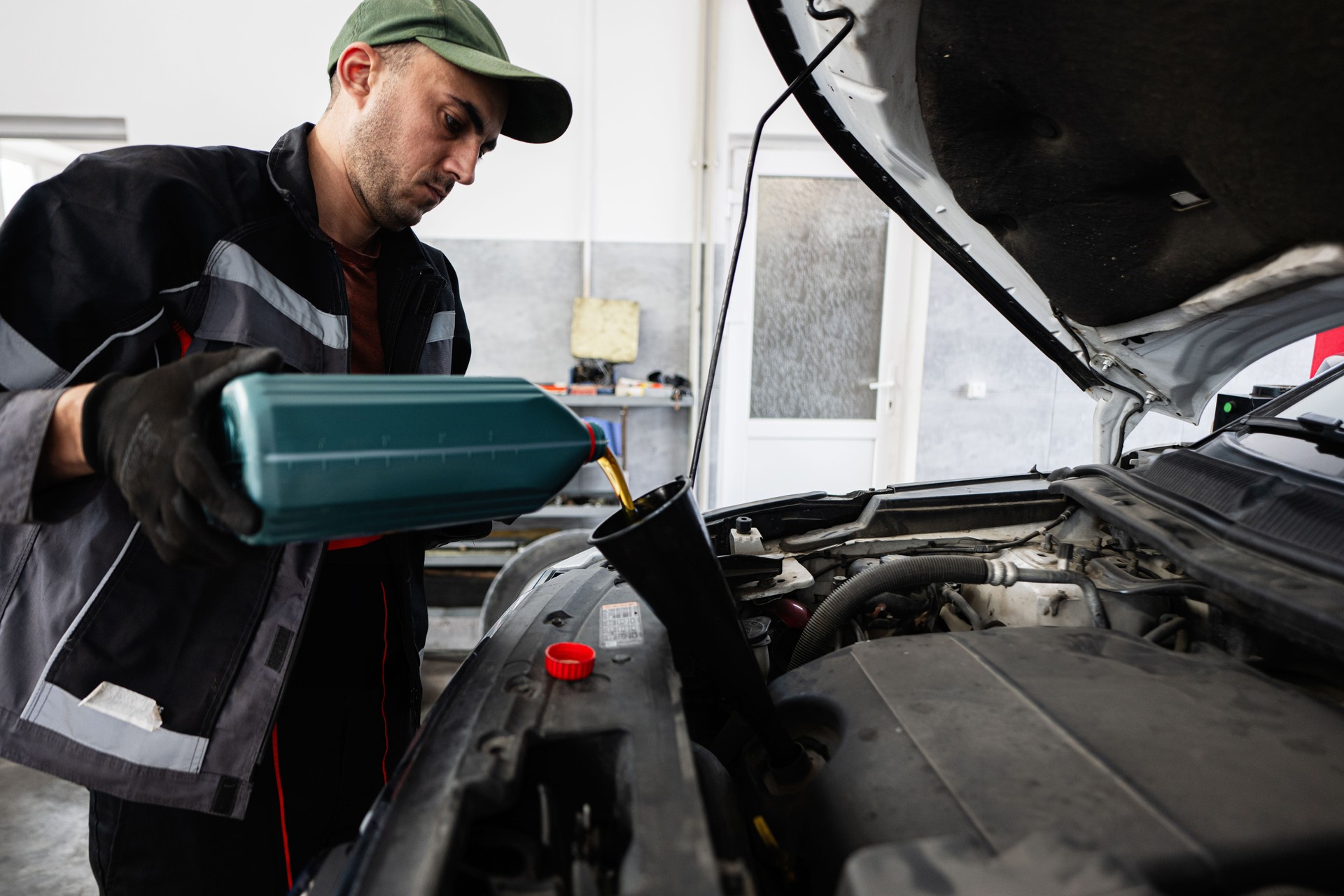 Mechanic pouring oil into car engine during maintenance service